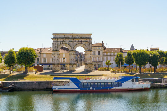 The ancient triumphal arch Arc de Germanicus in Saintes, France, photographed from the embankment of the Charente River. A blue and white ship stands by The weather is clear, the sky is blue