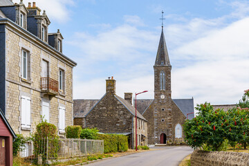 A small town with a church and a few houses in Brittany France. The houses are old and the church is tall. The sky is clear and the sun is shining