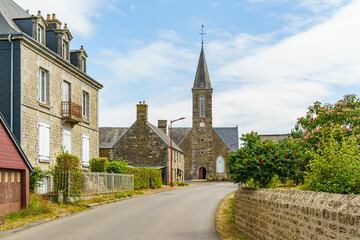 A small town with a church and a few houses in Brittany France. The houses are old and the church is tall. The sky is clear and the sun is shining
