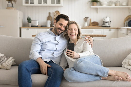 Loving couple cuddle on comfy couch take selfie using phone