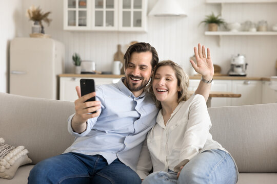 Happy couple sitting on couch communicating with friends by videocall - Powered by Adobe