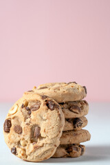 Vertical shot of freshly baked chocolate chip and nut cookies, with one cookie close up, showing texture. Pink background with copy space