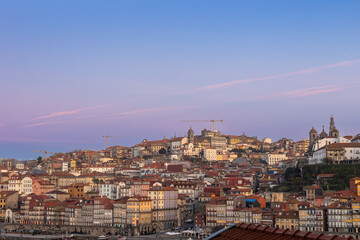 Obraz premium Colorful cityscape of Porto along the Douro River at sunset, featuring historic riverside buildings, traditional architecture, and a calm waterfront atmosphere in northern Portugal.