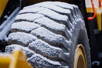 Detailed look at a thick winter coated construction vehicle tire displaying strong tread blocks and snow buildup commonly seen in cold industrial environments