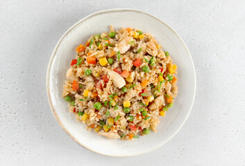Fried rice with chicken and vegetables carrots, peppers, corn, green peas on white background. Top view.