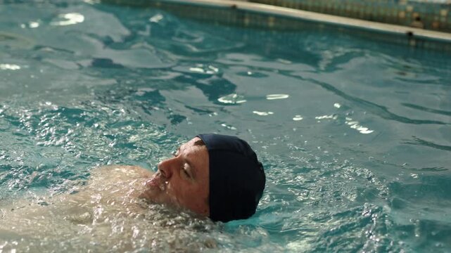overcoming challenges, rehabilitation pool, exercise environment. Man swimming with one arm, emphasizing overcoming physical challenges.