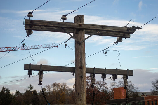 Wooden utility pole crossarms with ceramic insulators and power lines against a blue sky representing electrical infrastructure