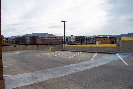 Empty concrete rooftop parking deck with a solitary light pole and a view of distant mountains and city buildings under a cloudy sky