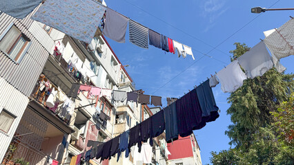Colorful laundry hangs across multiple clotheslines between old residential buildings under bright...