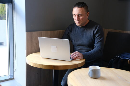 Handsome mature man sitting on sofa uses laptop while working at home. Remote working concept. Surf internet. High quality photo