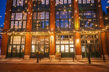 Fototapeta premium Historic brick building decorated with warm string lights in the Distillery District of Toronto during the evening.