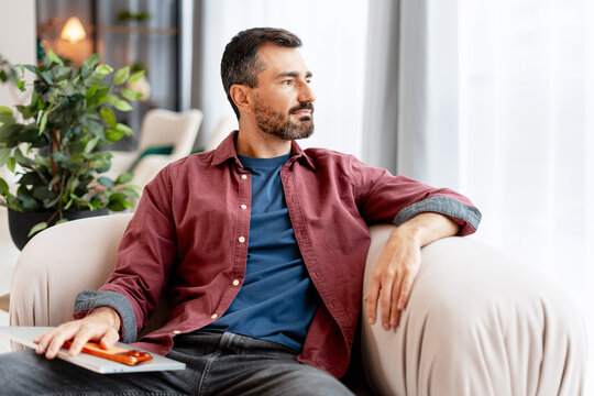 Thoughtful man relaxing in armchair at home looking away
