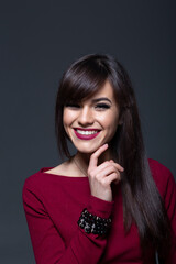 Studio Headshot of an Elegant Brunette Model with Dark Smokey Eyes and Serious Expression, Posing with Finger Near Chin and Wearing a Maroon Top on a Dark Grey Background