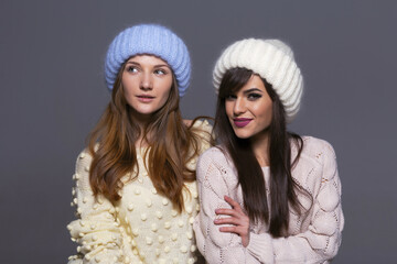 Waist-Up Shot of Two Female Models Displaying Warm Autumn or Winter Knitwear, Featuring a Blue Mohair Hat and Off-Shoulder Yellow Sweater Next to a White Ribbed Beanie and Patterned Beige Pullover