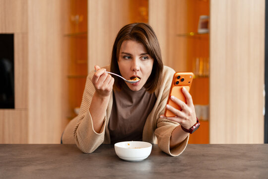 Young woman eating breakfast while using smartphone distracted