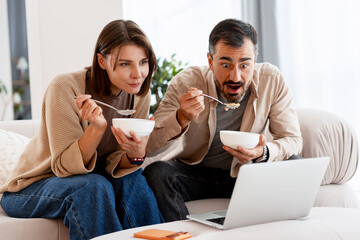 Couple eating breakfast watching shocking content on laptop