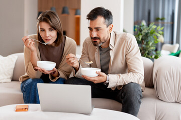 Couple eating breakfast cereal watching laptop together at home