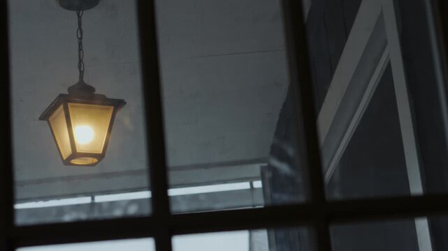 Illuminated porch light swaying on an ominous breeze. Filmed through an interior window.