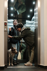 Two women stand in an elevator with a border collie on a leash. The scene reflects daily routine and the concept of urban living. © Ekaterina