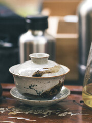 A lidded ceramic gaiwan with landscape painting rests on a floral-engraved wooden tray, ready for use in a traditional Chinese gongfu tea ritual.