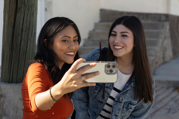 Happy young women taking a cheerful selfie together outdoors, capturing a moment of friendship and connection using a mobile phone, sharing joy and modern communication