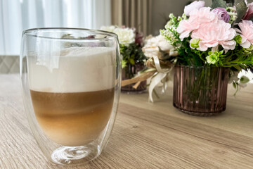 Creamy latte served in double walled glass with floral arrangements in the background