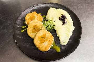 Savory pike cutlets with creamy mashed potatoes and fresh garnishes on a black plate