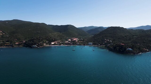 Aerial view of the coastline featuring lush green mountains and boats in the blue water, creating a beautiful contrast, Monte Argentario, Toscana, Italy.