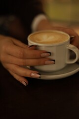 Close-up of a woman holding a coffee cup with beautifully manicured hands. A cozy lifestyle moment highlighting fashion, beauty, and elegance.