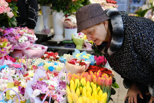 A Caucasian woman in a florist shop, taking notes at a counter, surrounded by various plants and flowers. She is smiling. High quality photo