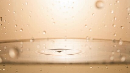 Close-up slow motion shot of a single water drop hitting a clear liquid surface creating ripples and splash in golden-toned light - Powered by Adobe