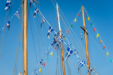 Abstract view of boat masts and rigging with colourful bunting and greek flags against a bright...