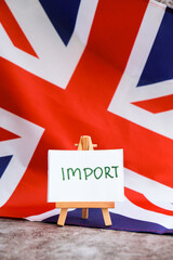 Paper note with words IMPORT on National symbol of Great Britain. British wave the UK silky flag background. Concept of economy industry global market international shipping