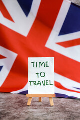 Paper note with words TIME TO TRAVEL on National symbol of Great Britain. British wave the UK silky flag background. Concept of travel destination tourism 