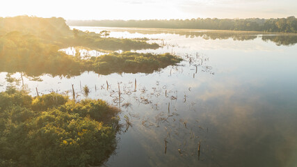 Drone view of Lake Valencia at dawn, with soft morning light over calm waters and the surrounding Amazon rainforest in Madre de Dios