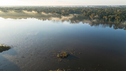 Drone view of Lake Valencia at dawn, with soft morning light over calm waters and the surrounding Amazon rainforest in Madre de Dios