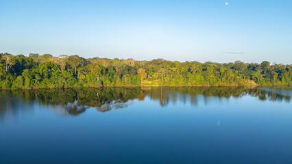 Drone view of Lake Valencia at dawn, with soft morning light over calm waters and the surrounding Amazon rainforest in Madre de Dios