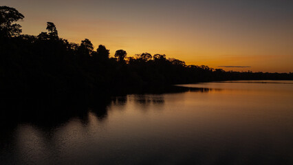Sunset at Lake Valencia with warm orange light reflecting on calm Amazon waters, surrounded by the lush rainforest of Madre de Dios