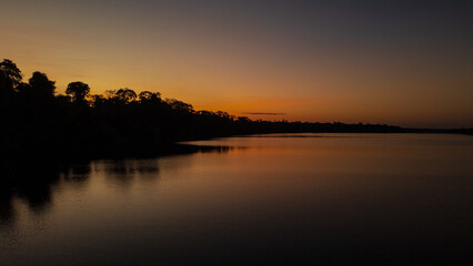 Sunset at Lake Valencia with warm orange light reflecting on calm Amazon waters, surrounded by the lush rainforest of Madre de Dios