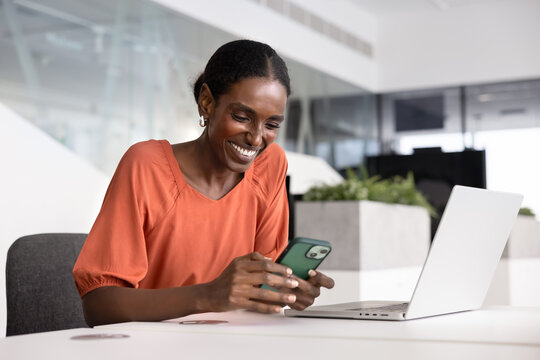 Cheerful young African business professional woman typing on smartphone