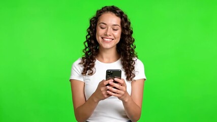 A cheerful woman holding a smartphone against a green background. - Powered by Adobe