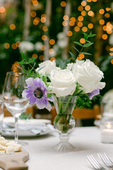 Elegant table setting with white roses and purple flowers surrounded by soft lighting at a romantic event