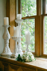 Candles and flowers decorate a sunlit window ledge in a cozy interior setting