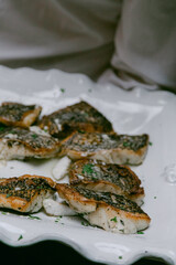 Grilled fish fillets served on a white plate with herbs in a cozy dining setting