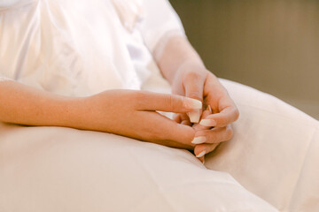 Elegant hands of a bride in a white gown sit patiently during a wedding ceremony at a serene location