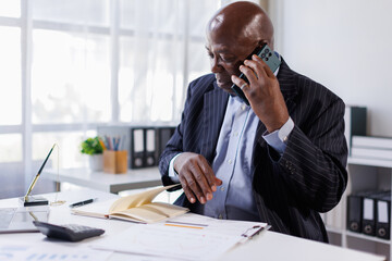 Senior manager, Senior businessman holding phone and working of analyzing documents and using laptop in the office.