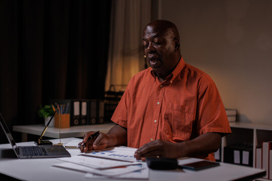Senior businessman working late at night in his office, Senior man sitting at desk and talking on mobile phone while checking graphs on laptop.
 - Powered by Adobe