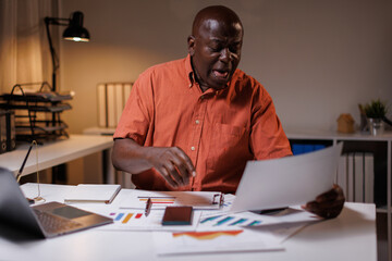 Senior businessman working late at night in his office, Senior man sitting at desk and talking on mobile phone while checking graphs on laptop.