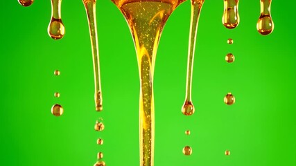Golden viscous liquid flows and drips against a vibrant green background creating a mesmerizing display of fluid dynamics and natural sweetness.