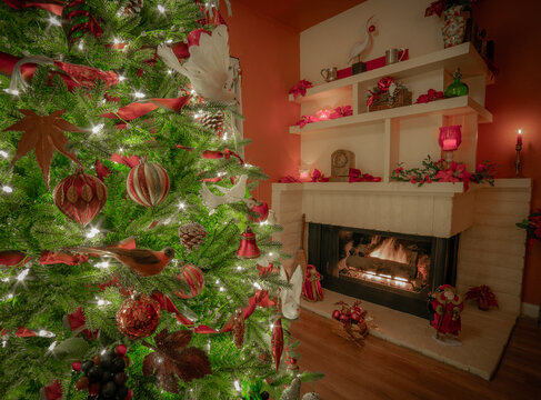 Christmas Tree stands in front of a burning log filled fireplace decorated in fruit and birds